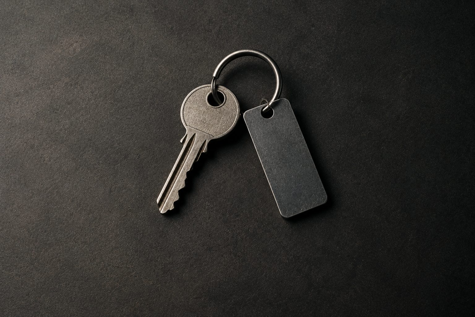 A single worn key on a ring with a blank metal tag, on a dark surface