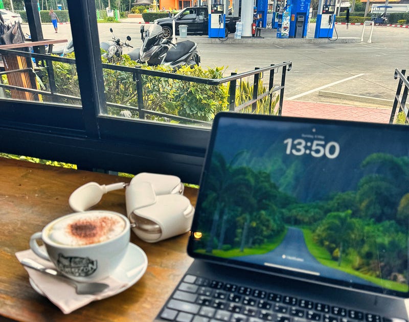 An iPad, headphones and a flat white on a wooden bench at a highway café, motorbike parked outside the window